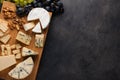 Tasting cheese dish on a wooden plate. Food for wine and romantic, cheese delicatessen on a dark stone table. Top view with copy s Royalty Free Stock Photo