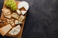 Tasting cheese dish on a wooden plate. Food for wine and romantic, cheese delicatessen on a dark stone table. Top view with copy s Royalty Free Stock Photo