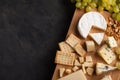 Tasting cheese dish on a wooden plate. Food for wine and romantic, cheese delicatessen on a dark stone table. Top view with copy s Royalty Free Stock Photo