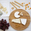 Tasting cheese with grapes, bread sticks, walnuts and pretzels over white wooden background, top view. Food for wine. Flat lay. Royalty Free Stock Photo