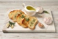 Tasty baguette with garlic, dill, rosemary and oil on white wooden table