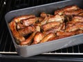 Tasty baked pork ribs in a black baking tray in an oven