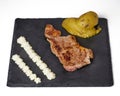 Beefsteak, Caliu potatoes and a spanish sauce called \'all i oli\' on a black slate board. Isolated over white