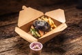 Tasty black burger takeaway in a box of recycled paper on wooden board