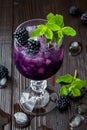 Tasty blackberry cocktail in wine glass with mint and ice on dark wooden table. Summer berry lemonade Royalty Free Stock Photo