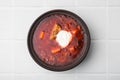 Tasty borscht with sour cream in bowl on white tiled table, top view