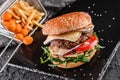 Tasty burger with cheese brie, blue cheese, mozzarella, tomatoes, arugula and fried stick balls, french fries on slate black Royalty Free Stock Photo