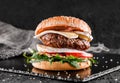 Tasty burger with cheese brie, blue cheese, mozzarella, tomatoes and arugula on slate black background, close up Royalty Free Stock Photo