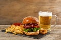 Tasty burger, French fries, fried onion rings and beer on wooden table. Fast food Royalty Free Stock Photo