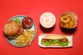 Tasty burger, French fries, hot dog, fried onion rings and refreshing drink on red background, flat lay. Fast food Royalty Free Stock Photo