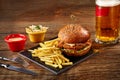 Tasty burger, french fries with sauce and glass of beer on black board Royalty Free Stock Photo