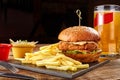 Tasty burger, french fries with sauce and glass of beer on black board Royalty Free Stock Photo