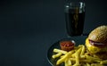 Tasty burger with french fries and tomato sauce near glass of cola on black background Royalty Free Stock Photo