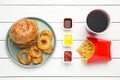 Tasty burger, fried onion rings, French fries, sauces and refreshing drink on white wooden table, flat lay. Fast food Royalty Free Stock Photo