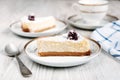 Tasty cheesecake with blackberry on a plate laying on a white wooden table with another cake and cup of coffee or tea on backgroun