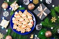Tasty Christmas cookies, gift boxes and decorations with Christmas tree and lights on black background. Royalty Free Stock Photo