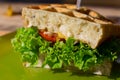 Tasty club sandwich with white waffle bread, tomato, onion, salad on green plate outdoor.