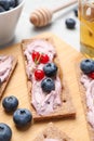 Tasty cracker sandwiches with cream cheese, blueberries, red currants, thyme and honey on wooden board, closeup