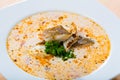 Tasty creamy soup with white fish cod and greens at white plate
