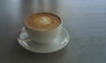 Tasty drinking, a cup of capuccino coffee decorated with heart pattern on brown milk froth in white ceramic cup on gray table