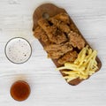 Tasty fast food: fried chicken drumsticks, spicy wings, French fries and chicken fingers with sour-sweet sauce and glass of cold Royalty Free Stock Photo
