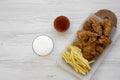 Tasty fast food: fried chicken drumsticks, spicy wings, French fries and chicken tenders with sour-sweet sauce and cold beer over Royalty Free Stock Photo