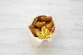 Tasty fast food: fried chicken legs, spicy wings, French fries and chicken fingers in paper box over white wooden background, top Royalty Free Stock Photo