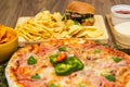 Tasty fast food on table. Pepperoni pizza and pizza Capricciosa , hamburger and potato chips Royalty Free Stock Photo