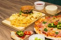 Tasty fast food on table. Pepperoni pizza and pizza Capricciosa , hamburger and potato chips Royalty Free Stock Photo