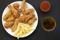 Tasty fastfood: fried chicken drumsticks, spicy wings, French fries, chicken fingers, glass of cold beer, sauce on white plate ove