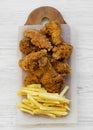 Tasty fastfood: fried chicken drumsticks, spicy wings, French fries and chicken tenders on rustic wooden board over white wooden Royalty Free Stock Photo