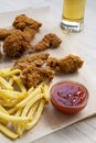 Tasty fastfood: fried chicken drumsticks, spicy wings, French fries and chicken strips with sour-sweet sauce and cold beer on a Royalty Free Stock Photo