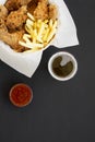 Tasty fastfood: fried chicken drumsticks, spicy wings, French fries and chicken tenders in paper box, sour-sweet sauce, cold beer Royalty Free Stock Photo