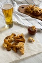 Tasty fastfood: fried potato wedges, chicken bites, barbecue sauce and glass of beer on a white wooden table, side view. Close-up