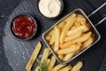 Tasty French fries, ketchup, rosemary and mayonnaise on black textured table, top view Royalty Free Stock Photo