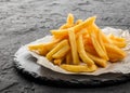 Tasty french fries potatoes on paper over black stone background. Hot fast food, close up Royalty Free Stock Photo