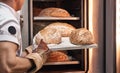 Tasty and fresh. Baker`s hands in working gloves taking out freshly baked bread from the oven at the kitchen