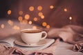 Tasty fresh cup of coffee on open paper book over Christmas lights close up. Royalty Free Stock Photo