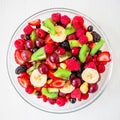 Tasty fresh fruit salad in glass plate on white wooden background. Flat lay. Top view. Royalty Free Stock Photo