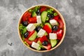 Horiatiki salad with chopped vegetables, lettuce, feta cheese and black olives in paper bowl on gray stone surface