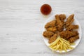 Tasty fried chicken legs, spicy wings, French fries, chicken tenders and sauce on white plate over white wooden background, top Royalty Free Stock Photo
