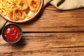 Tasty fried onion rings and french fries with ketchup on wooden table, flat lay. Space for text Royalty Free Stock Photo