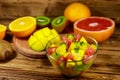 Tasty fruit salad in glass bowl and fresh fruits on wooden table Royalty Free Stock Photo