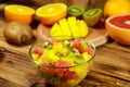 Tasty fruit salad in glass bowl and fresh fruits on wooden table Royalty Free Stock Photo