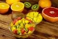 Tasty fruit salad in glass bowl and fresh fruits on wooden table Royalty Free Stock Photo