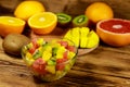 Tasty fruit salad in glass bowl and fresh fruits on wooden table Royalty Free Stock Photo