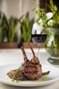 Tasty grilled lamb with herbs on a white plate against blurry glass of wine