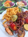 Grilled salmon and vegetables dish served with French fries and two bows of salad on a colorful table. Royalty Free Stock Photo