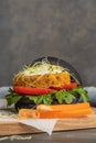Tasty grilled veggie burger with chickpeas and vegetables on black bread on wooden background Royalty Free Stock Photo