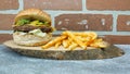 Tasty hamburger with cheddar cheese french fries, american salad and cucumber pickle on a natural wooden tray